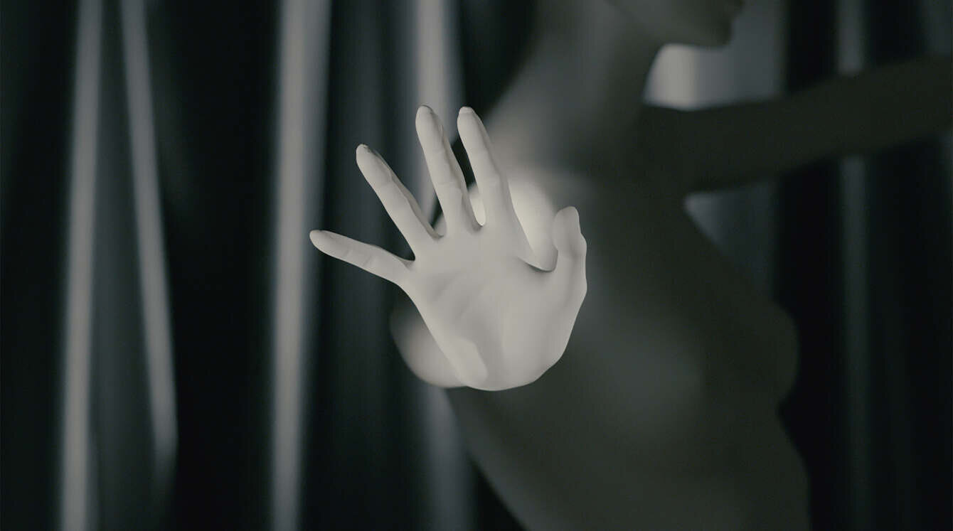 Still from Bustrofedico by Anna Franceschini: a pale hand held up toward the camera in front of dark curtains, a figure blurred behind it