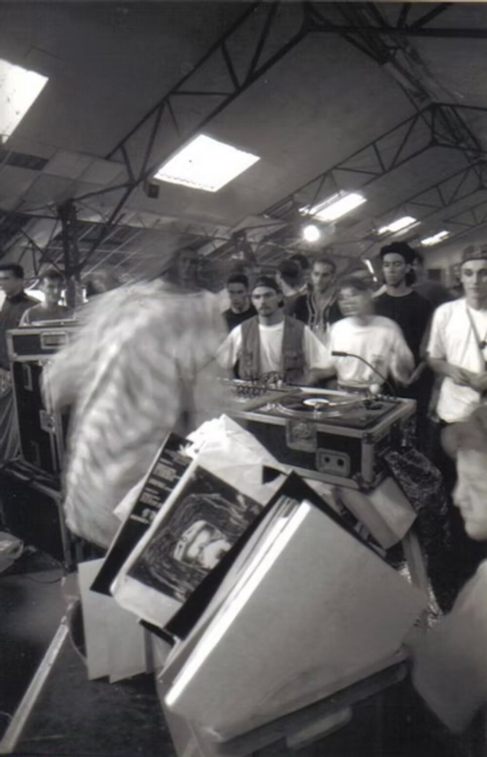 Black and white photo of a DJ at a rave, crowd behind the turntables