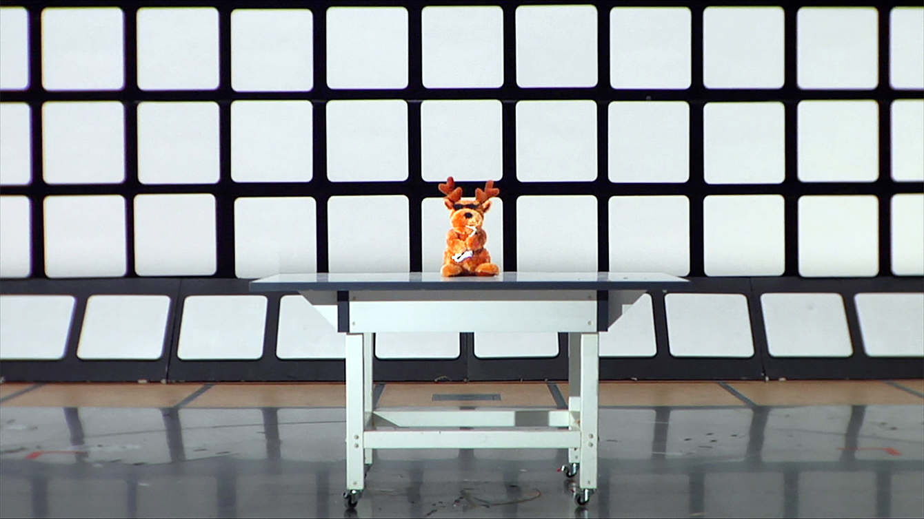 Still from What Time Is Love? by Anna Franceschini: a toy reindeer with sunglasses on a white table in front of a wall of white squares